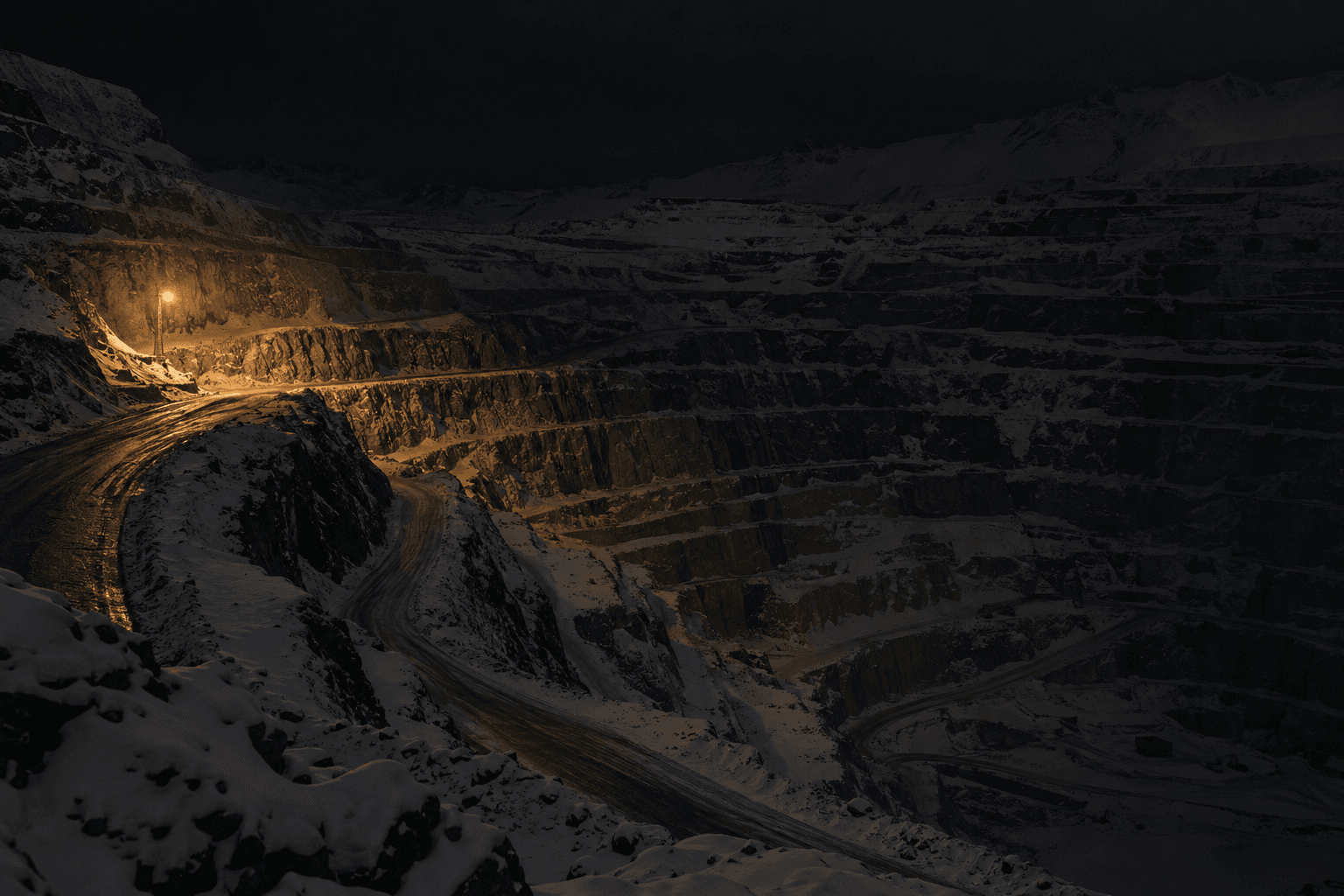 Snow covers the benches of a Chilean open-pit copper mine beneath a single work lamp.